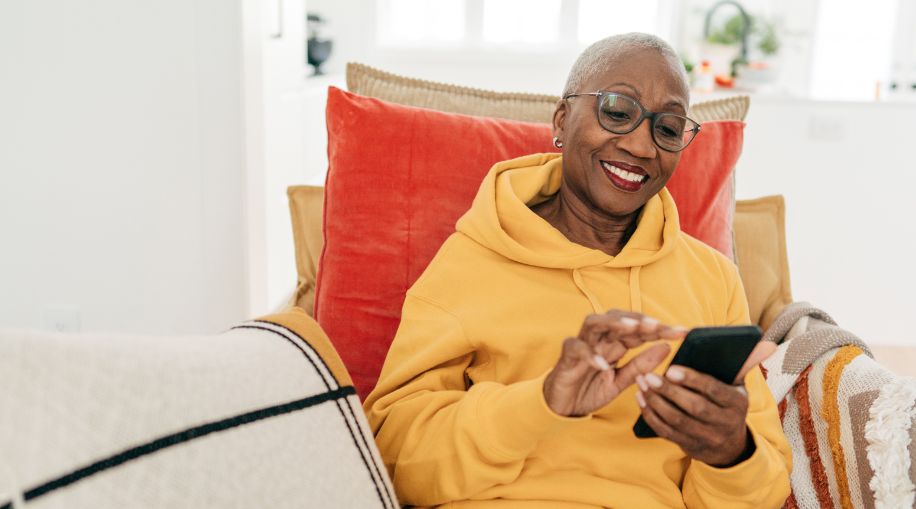 An older woman in a yellow sweater, sitting in a chair and holding a cell phone.